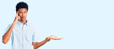 Genç Afro-Amerikalı bir adam günlük giysiler giymiş. Kafası karışmış ve avuç içi açık bir şekilde fotokopi alanı göstermekten rahatsız olmuş ve alnını işaret ediyor. Bunu bir düşün.. 