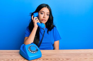 Güzel, esmer, genç bir kadın klasik bir telefonla konuşuyor. Düşünme tarzı ve ayık bir ifade. Kendine güveni var gibi. 