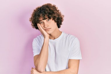 Yakışıklı, beyaz tişörtlü, yorgun ve bunalımda kollarını kavuşturmaktan sıkılmış görünen bir genç.. 