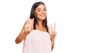 Gündelik kıyafetler giyen genç İspanyol kadın kameraya bakıp zafer işareti yapıyor. İki numara.. 