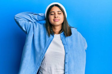 Hoş yün şapka takan, boynu ağrıyan, eli boynuna dokunan, kas ağrısı çeken genç Latin bir kadın. 