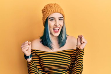 Yün şapka takan genç ve modern bir kız kollarını kaldırıp, gözleri açık bir şekilde başarıyı kutluyor. Kazanan konsept. 