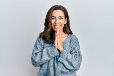 Genç esmer kadın, sıradan bir kazak giyip ellerinin birarada dua ederek af diliyor kendinden emin bir şekilde gülümsüyor.. 