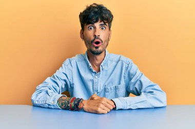 Gündelik kıyafetler giyen genç İspanyol adam masada korkmuş ve şok olmuş bir şekilde oturuyor.. 