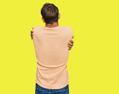 Sakallı, sıradan tişörtler giyen yakışıklı genç bir adam mutlu ve pozitif bir şekilde kendine sarılıyor. Sevgi ve özgüven. 