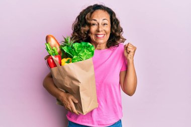 Orta yaşlı İspanyol kadın elinde ekmek ve bakkaliye torbalarıyla gururla bağırıyor zaferi ve başarıyı kutluyor. 