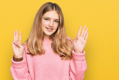 Güzel, genç, beyaz, sıradan bir kazak giyen ve 8 numaralı parmaklarıyla işaret eden, kendinden emin ve mutlu bir şekilde gülümseyen kız.. 