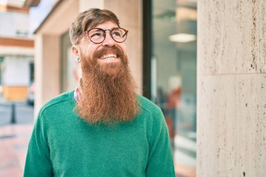 Kızıl sakallı genç İrlandalı adam şehirde mutlu bir şekilde yürürken gülümsüyor..