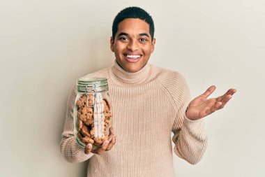 Genç, yakışıklı, İspanyol asıllı, elinde bir kavanoz çikolata parçalı kurabiye tutan mutlu bir gülümsemeyle zaferi kutlayan ve elini kaldıran bir adam. 