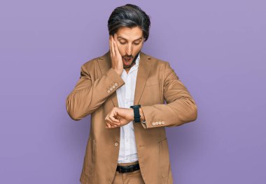 Latin kökenli genç adam iş kıyafetleri giyiyor. Saate bakıyor. Endişeli, geç kalmaktan korkuyor. 