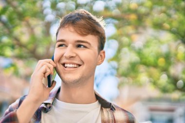 Genç beyaz adam gülümsüyor. Şehirdeki akıllı telefondan konuşuyor..