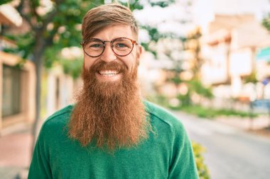 Kızıl sakallı genç İrlandalı adam şehirde mutlu bir şekilde yürürken gülümsüyor..