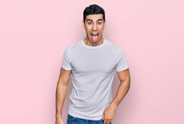 Beyaz tişört giyen yakışıklı İspanyol adam komik bir ifadeyle dilini dışarı çıkarıyor. duygu kavramı. 