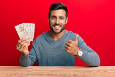 Yakışıklı İspanyol adam Birleşik Krallık 'ı elinde tutuyor mutlu ve pozitif gülümsüyor, başparmağıyla mükemmel ve onay işareti yapıyor. 