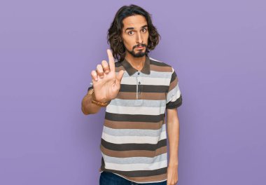 Latin asıllı genç bir adam, gündelik giysiler giyip parmağını kaldırmış ve kızgın bir ifade takınıyor. 
