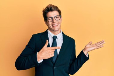 İş elbisesi giymiş yakışıklı beyaz adam hayret içinde kameraya bakıp gülümserken eliyle ve parmağıyla işaret ediyor.. 