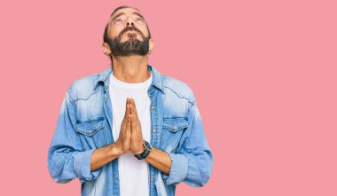 Uzun saçlı ve sakallı çekici bir adam sıradan bir kot ceket giyiyor, elleri bağlı yalvarıyor ve dua ediyor. Yüzünde umut ifadesi var. Çok duygusal ve endişeli. Yalvarıyor. 