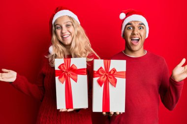 Irklar arası genç çift Noel şapkası takıyor ve bir hediye tutuyor başarıyı mutlu bir gülümsemeyle kutluyorlar ve kazanan yüz ifadesini kaldırarak. 