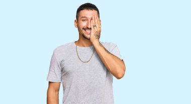 90 'ların tarzında dövmeleri olan yakışıklı bir adam bir gözünü eliyle kapatıyor, yüzünde kendine güvenen bir gülümseme ve şaşırtıcı bir duygu var.. 