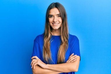 Gündelik kıyafetler giyen, kollarını kavuşturup kameraya gülümseyen genç İspanyol kadın. pozitif kişi. 