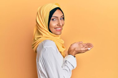 Genç esmer Arap kadın geleneksel İslami başörtüsü takıyor. Avuç içleri açık, fotokopi alanını gösteren, heyecanlı mutlu bir gülümseme gösteren bir eşarp. 