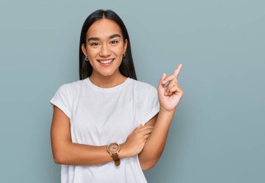 Yüzünde kocaman bir gülümseme olan sıradan beyaz tişört giyen genç Asyalı kadın, kameraya el ve parmak ile bakıyor.. 