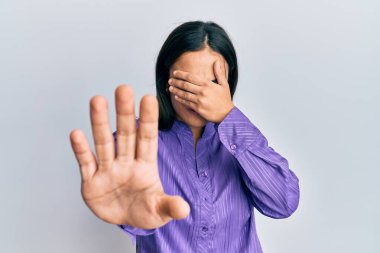 Genç esmer kadın gündelik giysiler giyip ellerle gözlerini kapatıyor ve üzgün ve korku ifadeleriyle jest yapıyor. utangaç ve olumsuz kavram. 