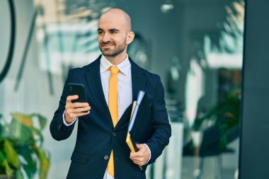 Genç Latin kökenli kel iş adamı şehirde akıllı telefon kullanarak mutlu bir şekilde gülümsüyor..