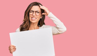 Elinde boş afiş tutan genç esmer kadın elleri kafasında, şaşırmış ve sinirli yüzüyle stresli ve hayal kırıklığına uğramış. 