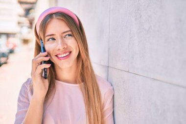 Kafkasyalı genç kız gülümsüyor. Duvara yaslanmış akıllı telefondan konuşuyor..