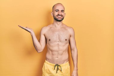 Mayo giyen genç kel adam gülümseyen neşeli bir sunum yapıyor ve avuç içi kameraya bakıyor.. 