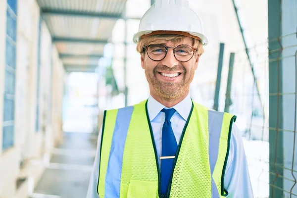 Business architect man wearing hardhat standing outdoors of a building project wearing reflective vest