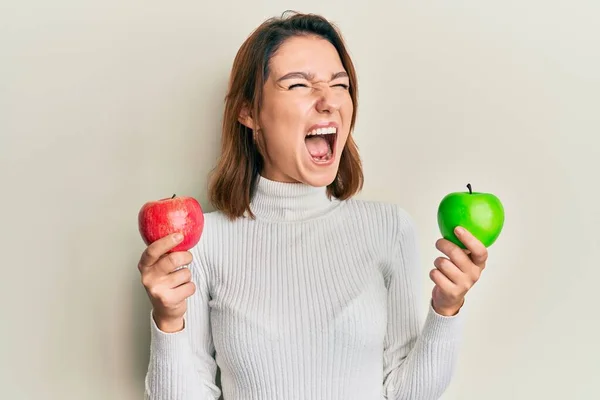 Joven Mujer Caucásica Sosteniendo Manzana Roja Verde Enojada Loca Gritando — Foto de Stock