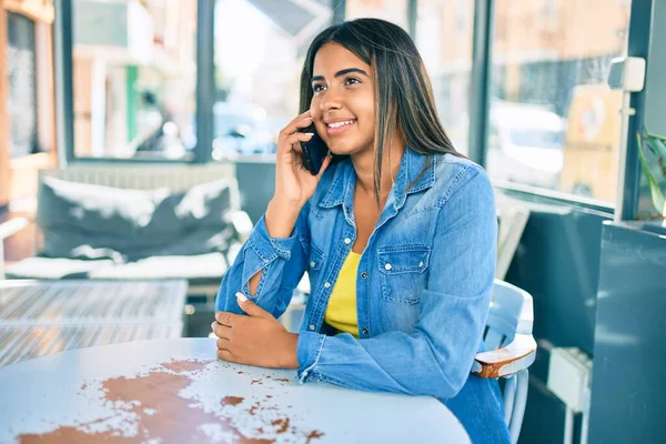 Young latin woman smiling happy talking on the smartphone at coffee shop terrace.