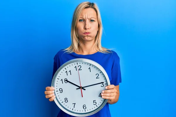 Beautiful Middle Age Blonde Woman Holding Big Clock Puffing Cheeks — Stock Photo, Image