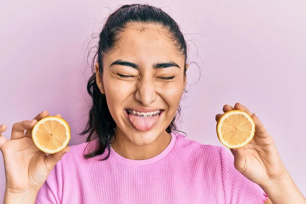 西班牙裔少女 带着牙套 手里拿着柠檬 伸出舌头 带着滑稽的表情 高兴极了 — 图库照片
