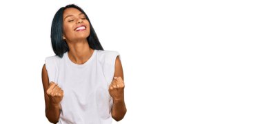 Başarı için heyecanlı, kollarını kaldırmış ve gözleri kapalı zaferi kutlayan gündelik giysiler giyen genç Afro-Amerikalı kadın. Kazanan konsept. 