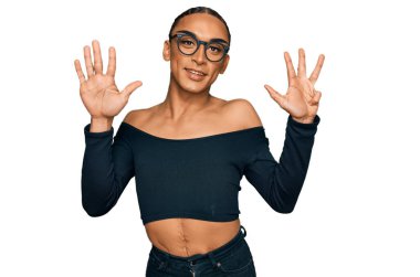 Makyaj yapan, uzun saçlı, kadın kıyafetleri giyen İspanyol transseksüel adam dokuz numarayı gösterip gülümseyerek mutlu ve kendinden emin bir şekilde işaret ediyor.. 