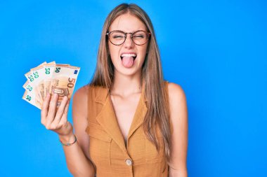 Avro banknotları tutan genç sarışın kız komik bir ifadeyle dilini dışarı çıkarıyor.. 