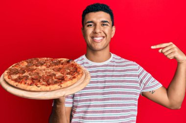 Genç bir Arap, İtalyan pizzasını tutarken gülümseyen mutlu ve gururlu birini işaret ediyor. 