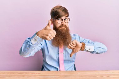 Genç İrlandalı kızıl saçlı, iş gömleği ve kravat takmış masanın üzerinde oturmuş, baş parmak işareti yapıyor, anlaşmazlık ve uzlaşma ifadesi. çılgın çatışma 