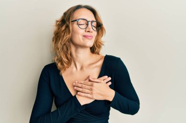 İş gömleği ve gözlük takan, elleri göğsünde, gözleri kapalı gülümseyen ve yüzünde minnet ifadesi olan beyaz bir kadın. sağlık kavramı. 