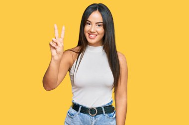 Gündelik kıyafetler giyen genç ve güzel İspanyol kız iki numarayı gösterip işaret ederken kendinden emin ve mutlu bir şekilde gülümsüyor.. 