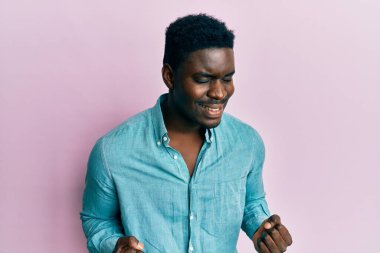 Yakışıklı siyah adam gündelik kıyafetler giyiyor çok mutlu ve heyecanlı kolları havada, gülümseyen ve başarı için çığlık atan kazanan bir jest yapıyor. kutlama konsepti. 