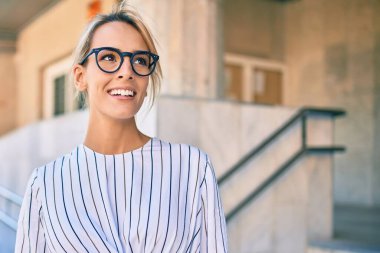 Genç sarışın iş kadını gülümseyerek şehirde mutlu mesut yürüyor..