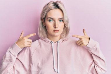 Genç sarışın kız dudaklarını işaret ediyor parmakları gevşemiş ve yüzünde ciddi bir ifade var. Basit ve doğal bir şekilde kameraya bakıyorsun.. 