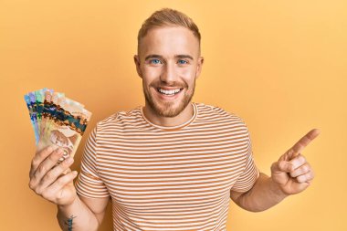 Kanadalı genç beyaz adam elinde dolarlarla mutlu bir şekilde gülümsüyor. 