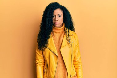 Orta yaşlı Afro-Amerikalı kadın yün kazak ve deri ceket giyiyor. Yüzünde ciddi bir ifade var. Basit ve doğal bir şekilde kameraya bakıyorsun.. 