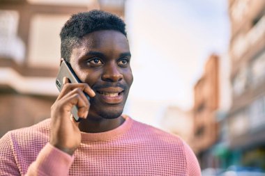 Genç Afrikalı Amerikalı gülümseyen mutlu bir adam şehirdeki akıllı telefondan konuşuyor..