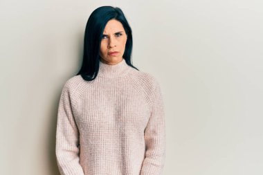 Gündelik kışlık süveter giyen, kuşkucu ve gergin genç beyaz bir kadın. Yüzünde çapraz kollarla onaylamayan bir ifade var. negatif kişi. 